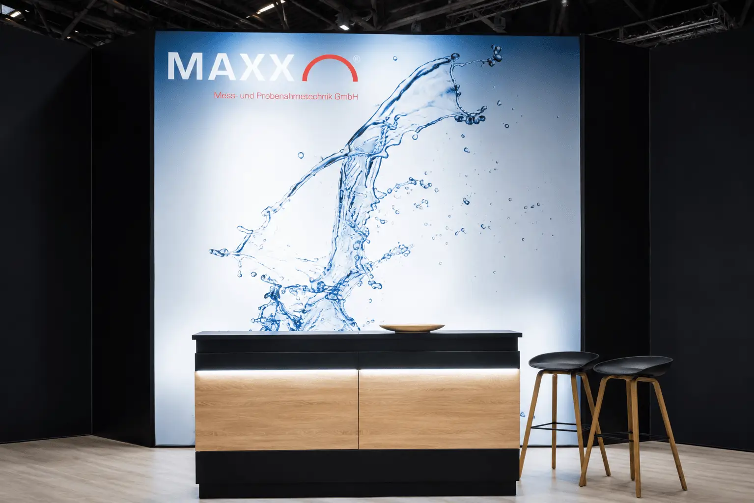 Messestand MAXX GmbH IFAT München 2026 – Empfangstresen mit hinterleuchteter Wasserspritz-Grafik, Expoline Messebau.